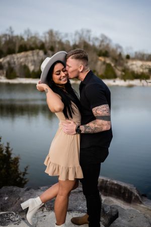 Couple sharing romantic moments on rocky lakeside during overcast day.