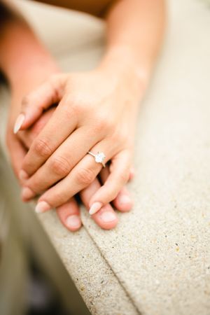 Close-up shots of hands resting on textured stone surface with engagement ring.