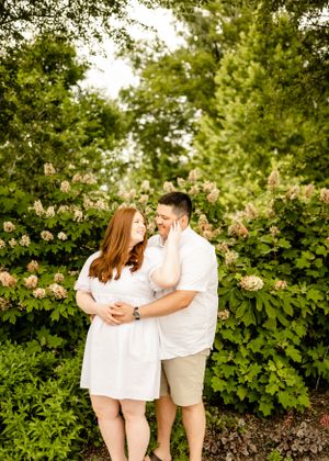 Romantic couple embracing among blooming rose bushes and greenery.
