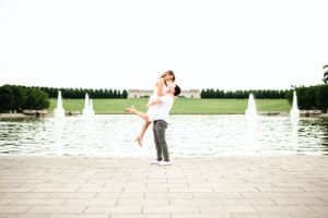 Wide panoramic view of couple on stone terrace with lake and gardens in background.