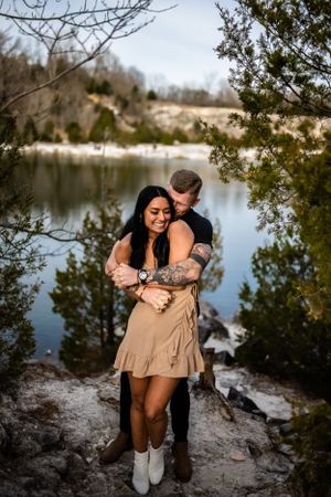 Couple embracing and laughing together on rocky shore with lake view.
