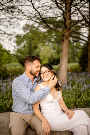 Romantic engagement photos in garden setting with blooming purple flowers.