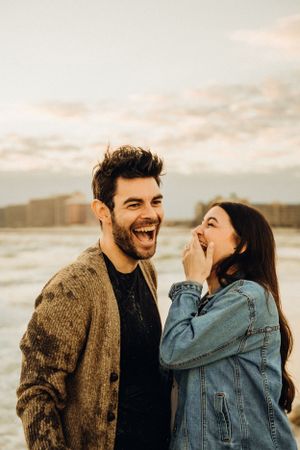 A couple sharing joyful laughter while embracing on a beach at sunset.
