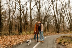 A couple walking together on a leaf-covered path beneath bare winter trees.