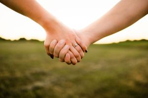 Two hands clasped together against a sunset backdrop in a field.