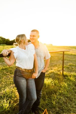 A couple laughs together in a sun-drenched field during golden hour.