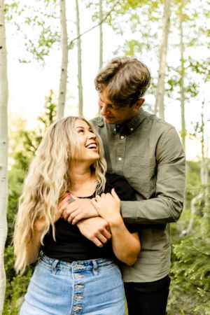 Casual couple sharing laughter and embraces among birch trees.