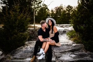 A couple shares a romantic moment on snowy rocks surrounded by evergreen trees.