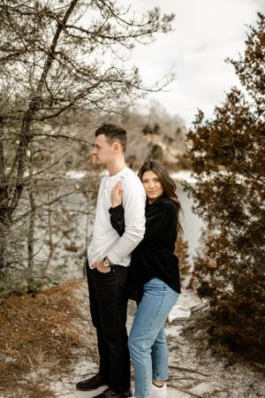 A couple stands together on a rocky outcrop surrounded by winter foliage.