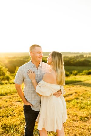 A romantic couple embraces in a golden field during sunset.