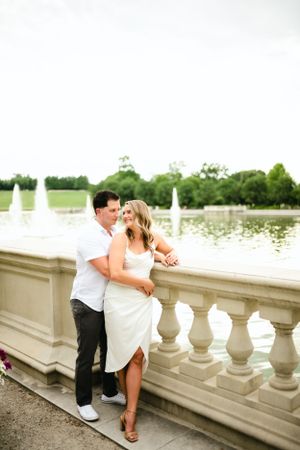 Couple in white outfits sharing romantic moments along a stone balustrade overlooking a lake.