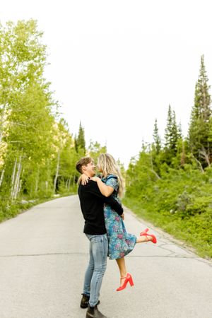 Playful couple sharing romantic moments on a mountain road surrounded by evergreen trees.