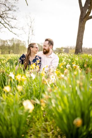 Couple embracing in a meadow filled with yellow daffodils and bare trees.
