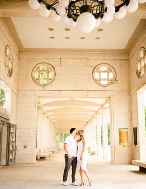 A couple poses in an elegant colonnade with white globe lights overhead.