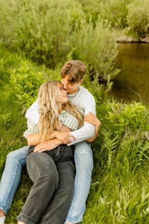 Intimate moments shared between couple sitting in tall grass by a stream.