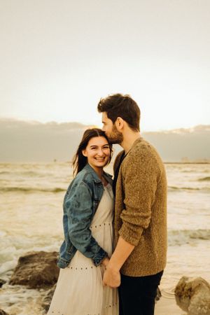 A couple in casual attire sharing intimate moments and laughter by the ocean.