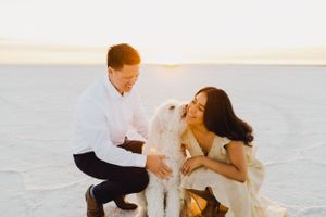 Playful couple interacts with their white dog during sunset photoshoot on salt flats.