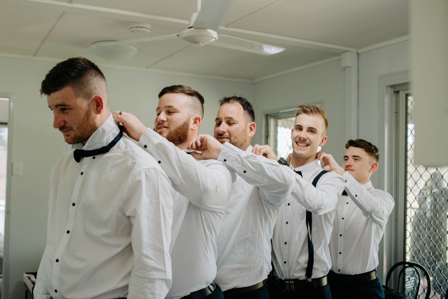 Groomsmen in white shirts pose in a line doing a domino effect photo.