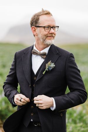Groom in classic dark suit and bowtie with boutonniere during outdoor wedding.