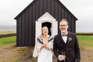 A couple celebrates outside a black and white Nordic-style chapel on a misty day.
