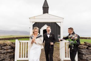 A wedding ceremony takes place outside a charming black and white chapel in the countryside.