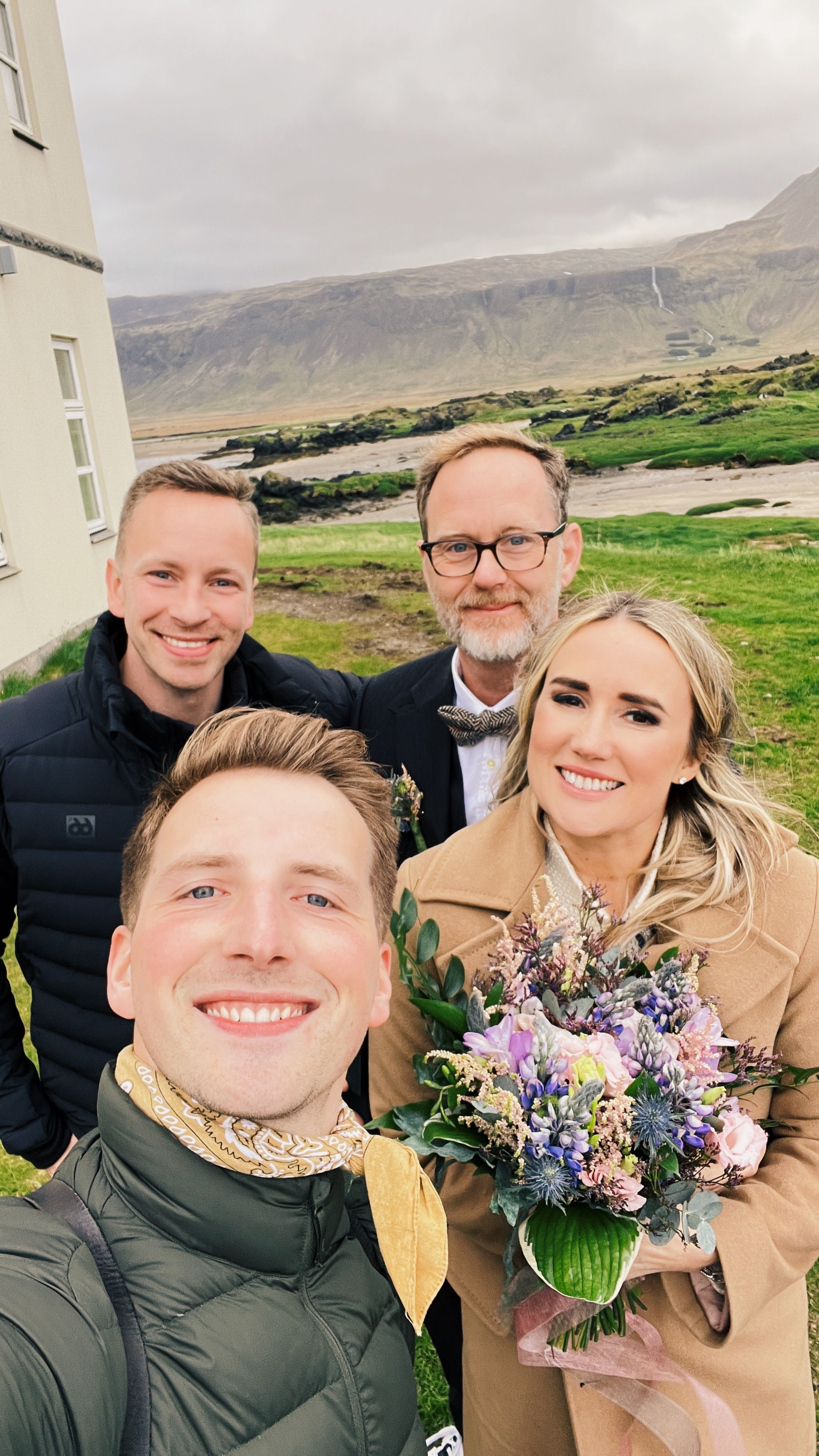 Wedding celebration group with colorful bouquet against dramatic mountain landscape.