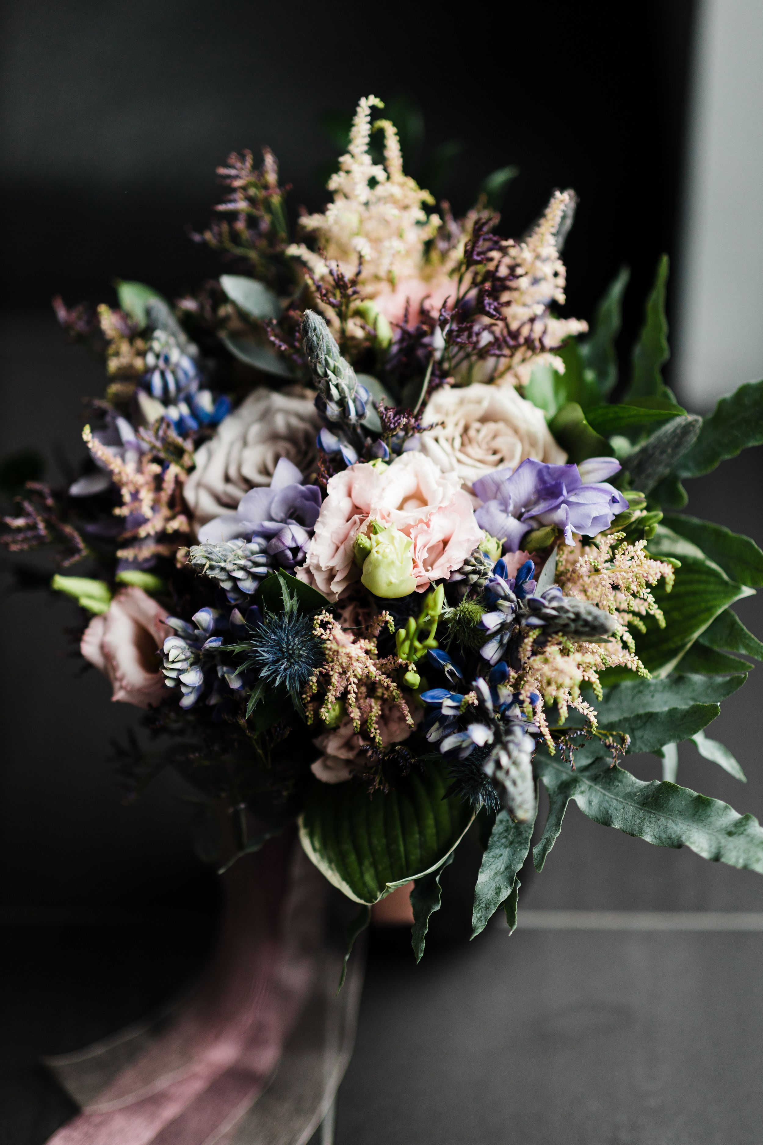 Moody wedding bouquet with purple, pink and white flowers against dark background.