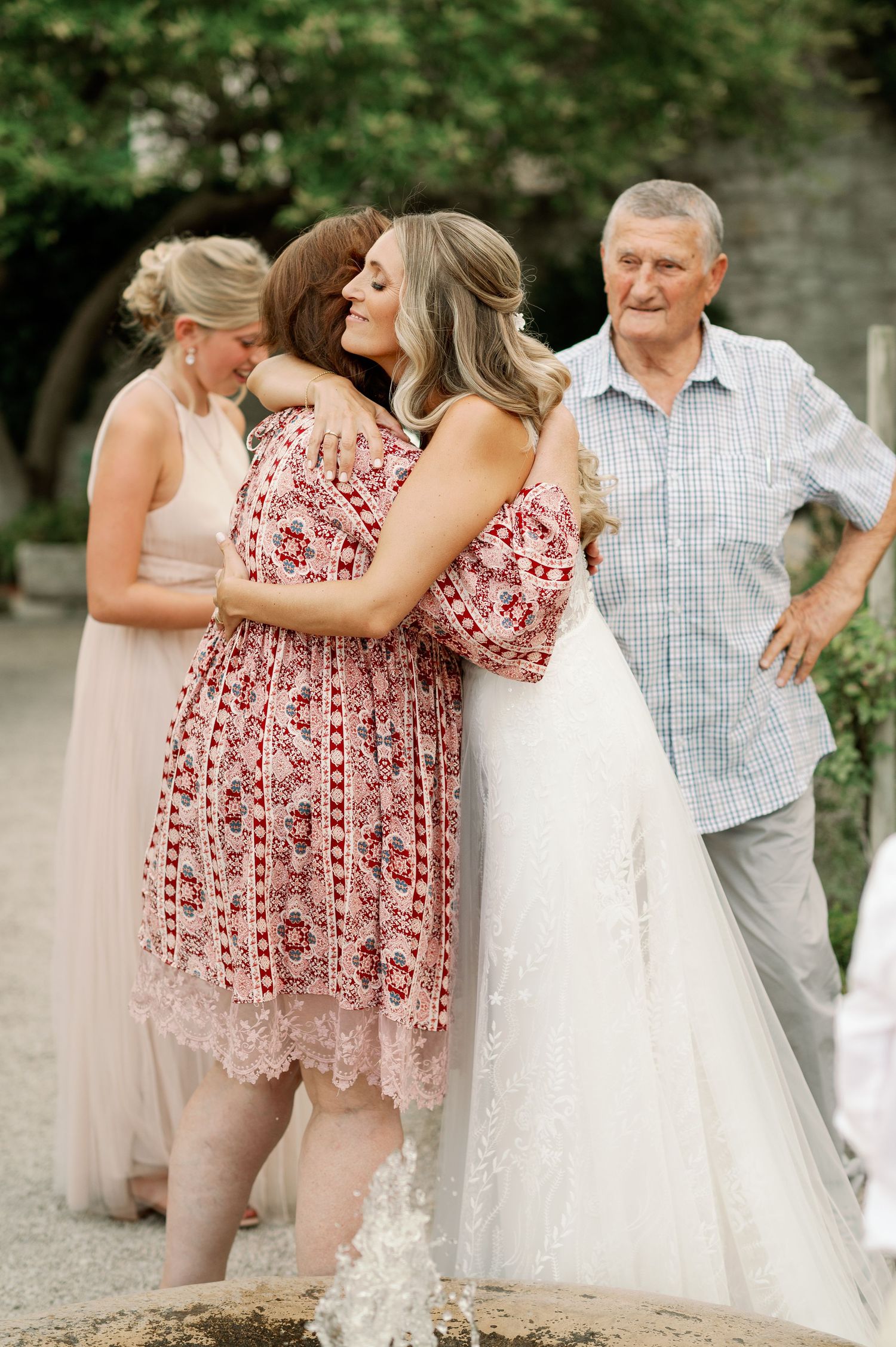 Heartfelt embrace between wedding guests in floral dress and bride in garden setting.
