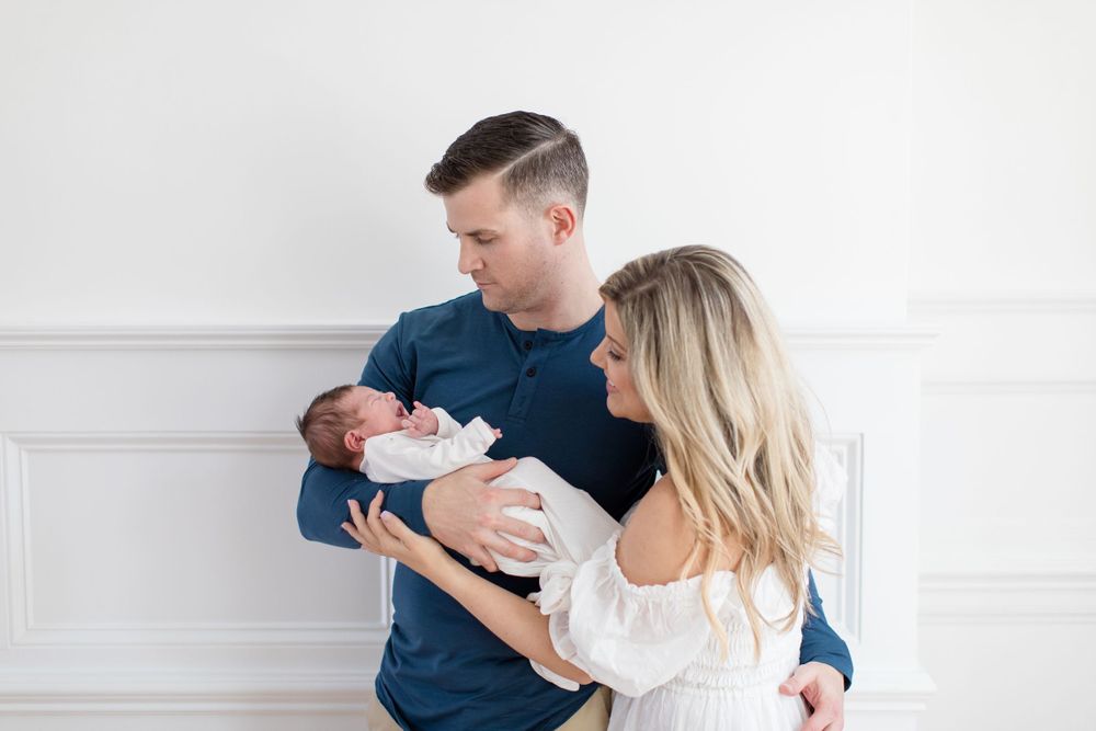 Parents in navy and white outfits tenderly holding their newborn baby together.