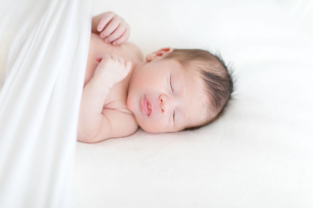 Peaceful sleeping newborn baby lying on white blanket with arms raised.