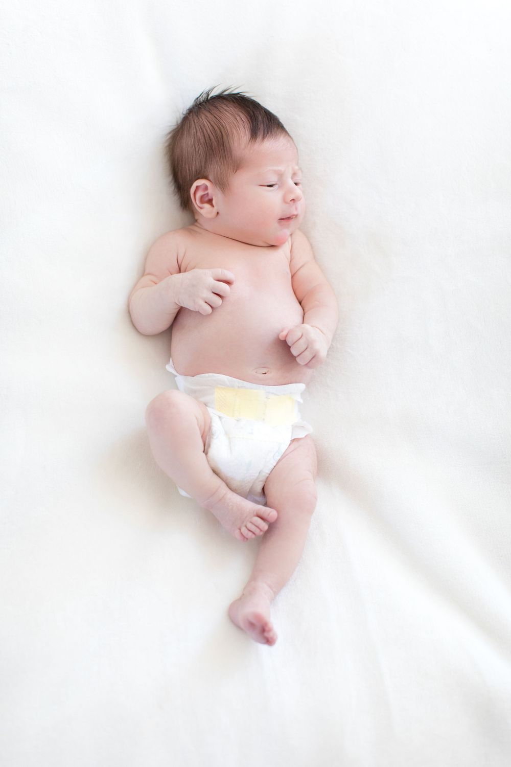 Newborn baby wearing diaper resting on soft white fabric.