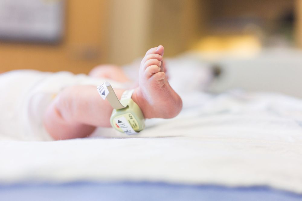 Close-up of tiny newborn baby feet with hospital ID tag against white bedding.