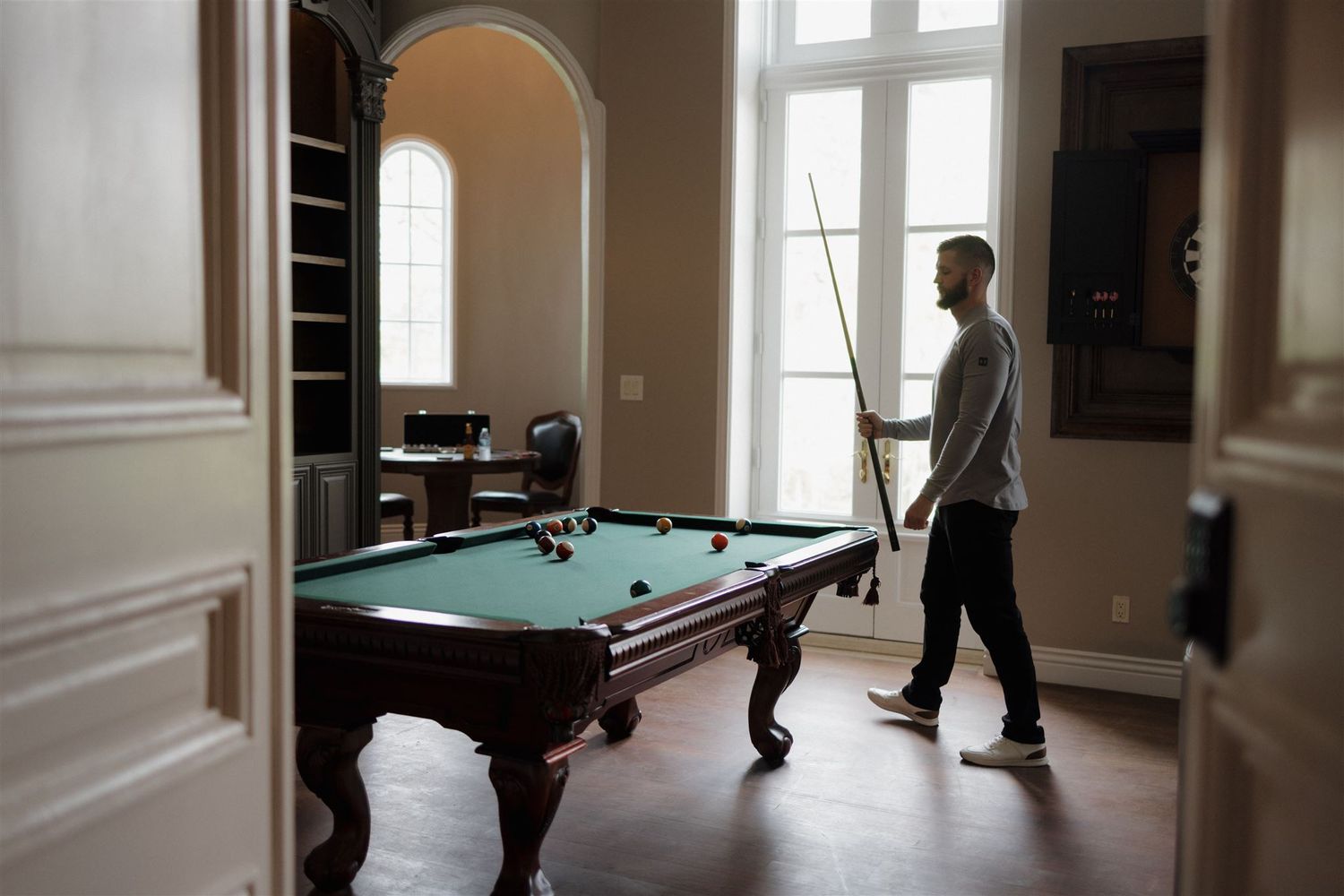 Person standing near a pool table in an elegant room with arched doorways and tall windows.