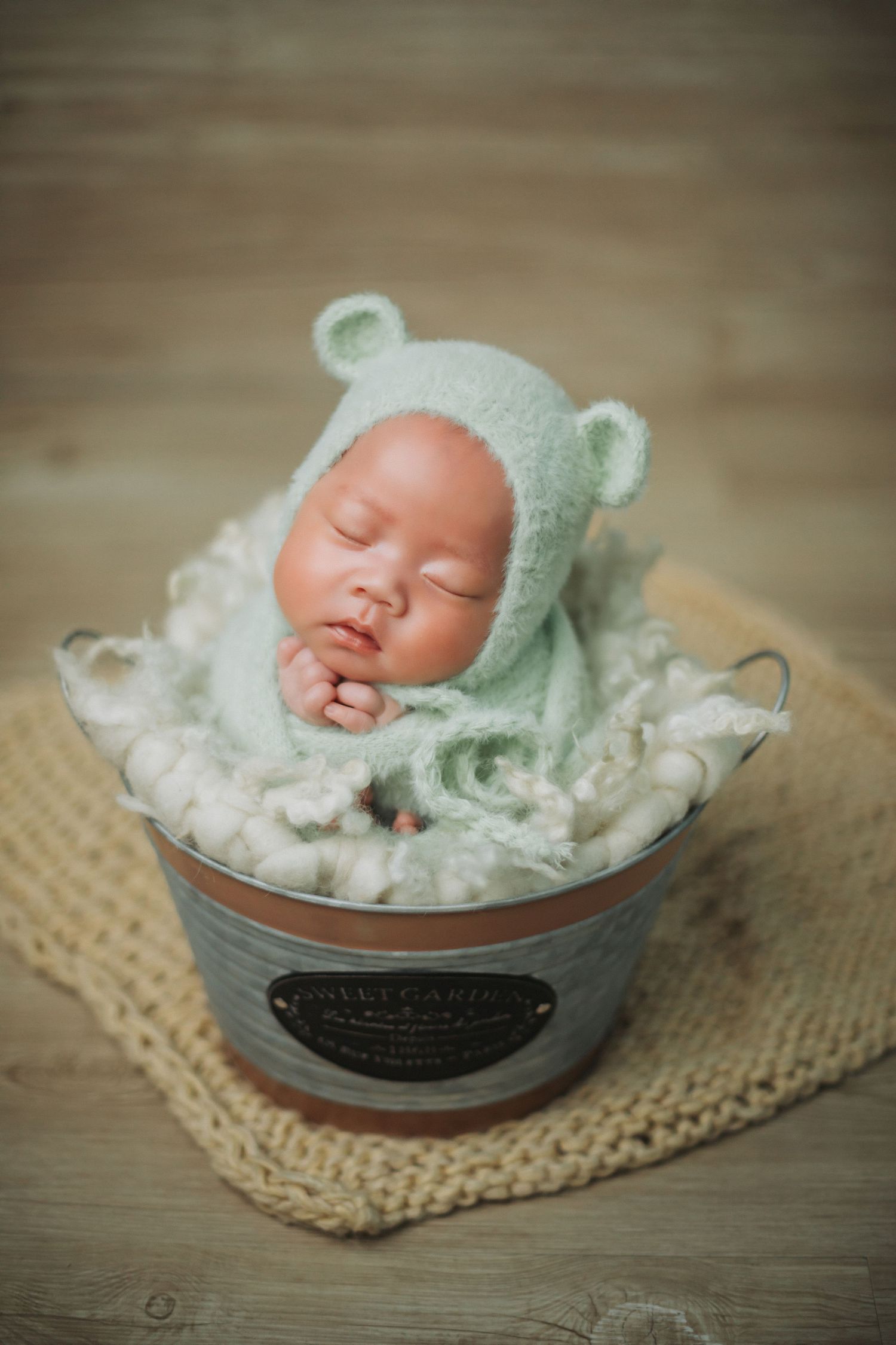 Newborn baby in mint green bear bonnet and wrap sleeping in a rustic metal bucket.