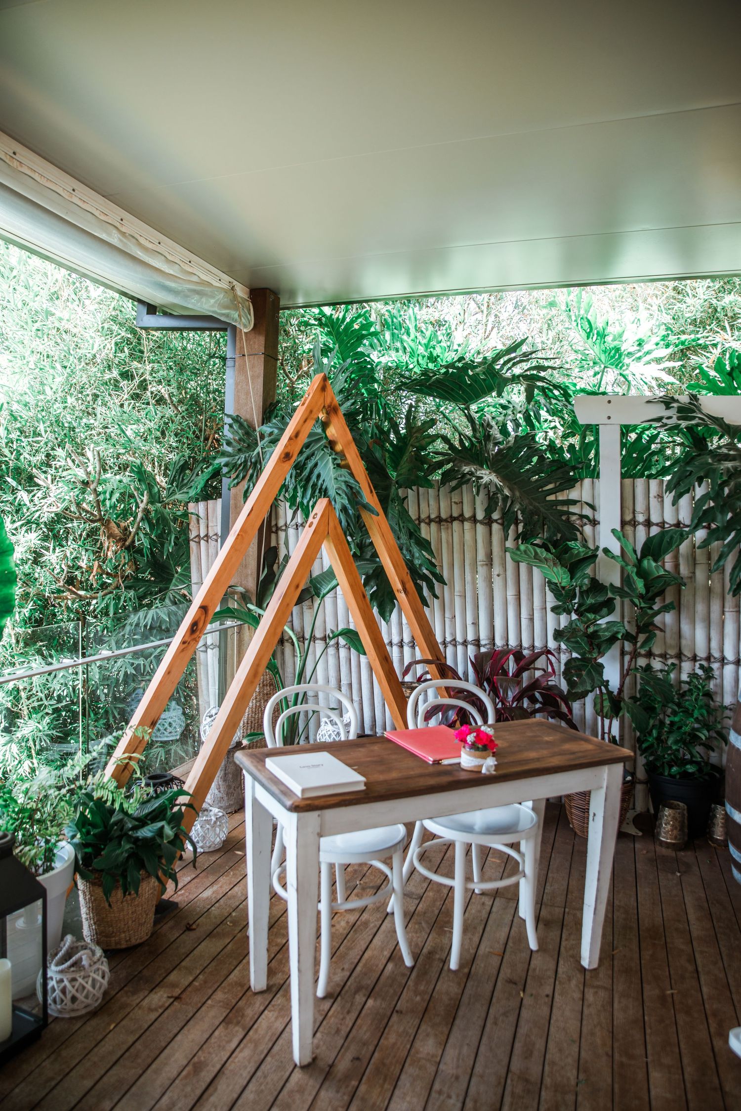 Outdoor patio deck decorated with plants and a wooden A-frame structure near a white dining table and chairs.