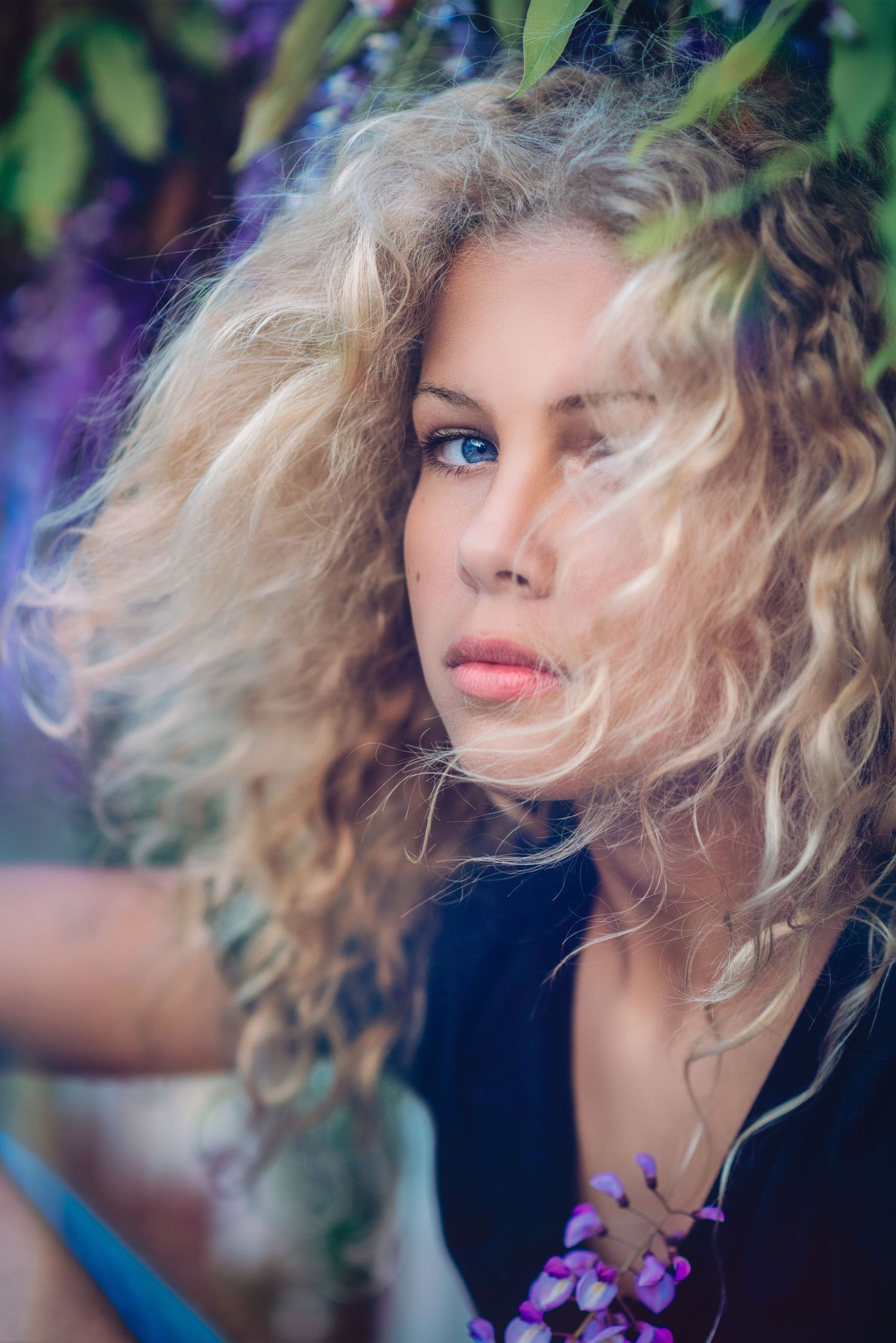Artistic portrait with blonde curls framed by purple flowers and foliage.