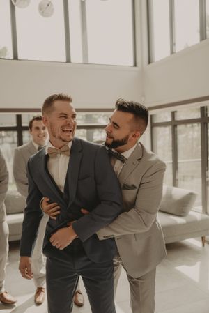 Groomsmen share playful moment in modern space with natural lighting.