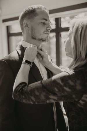 Final wedding preparations as tie is adjusted in natural window light.