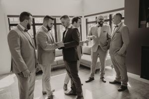 Groomsmen in light colored suits gathered together in casual conversation before a wedding ceremony.
