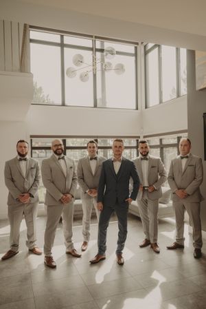Candid moment of laughter and joy between groomsmen in formal attire at wedding venue.