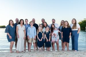Group portrait of people wearing blue and white clothes on a beach at sunset.