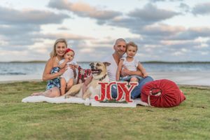 Family picnic scene on beach grass at sunset with JOY sign and red pillows.