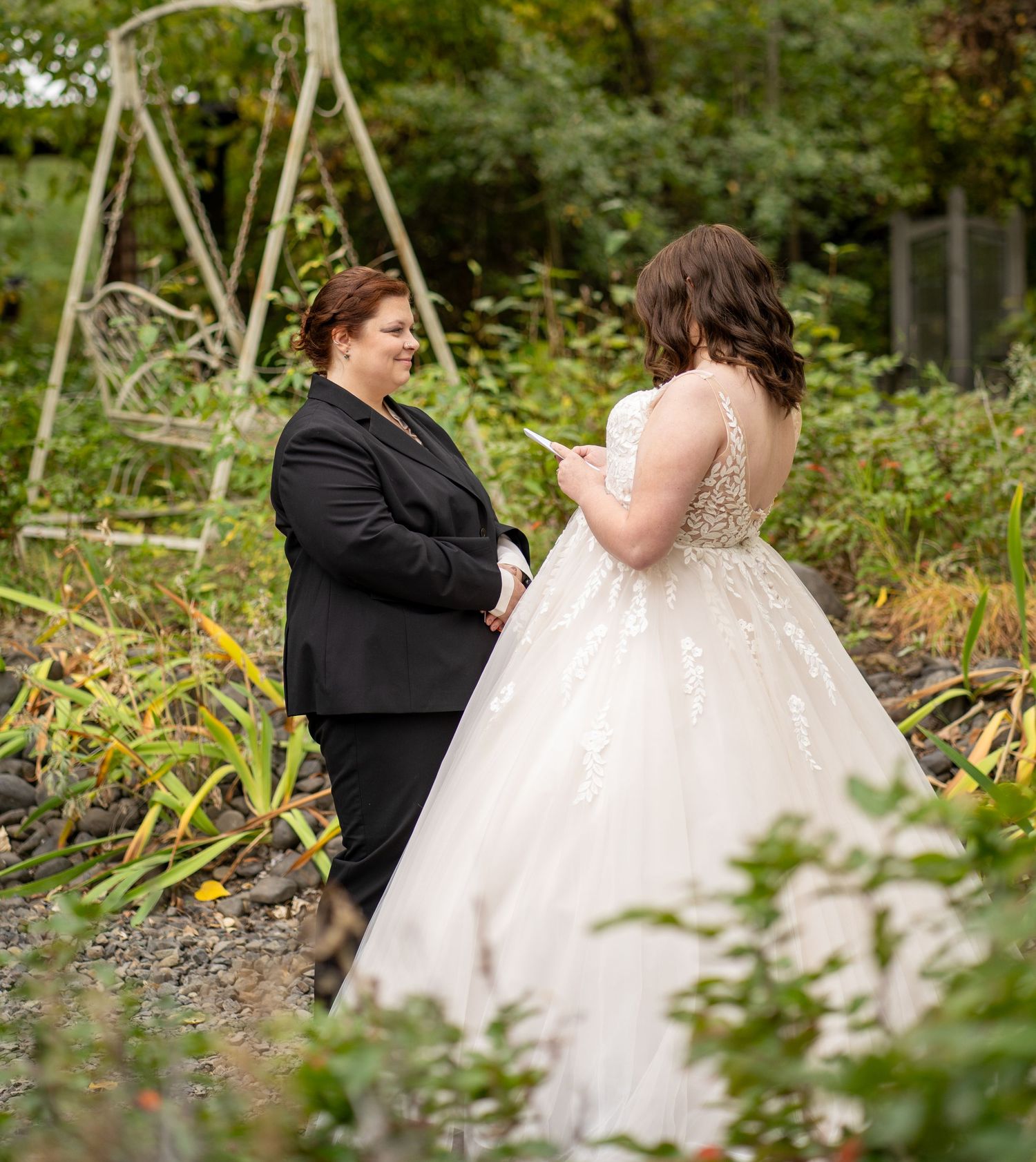 Two people share vows in a garden setting surrounded by autumn foliage.
