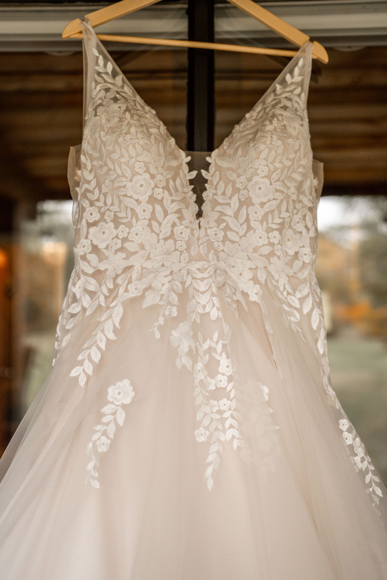 A detailed wedding dress with intricate lace pattern hangs on display.
