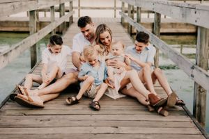 A family sits together laughing and playing on a wooden dock by the water.