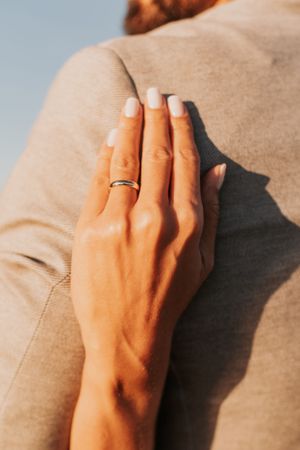 Close-up of a hand with wedding ring resting on a beige suit jacket.