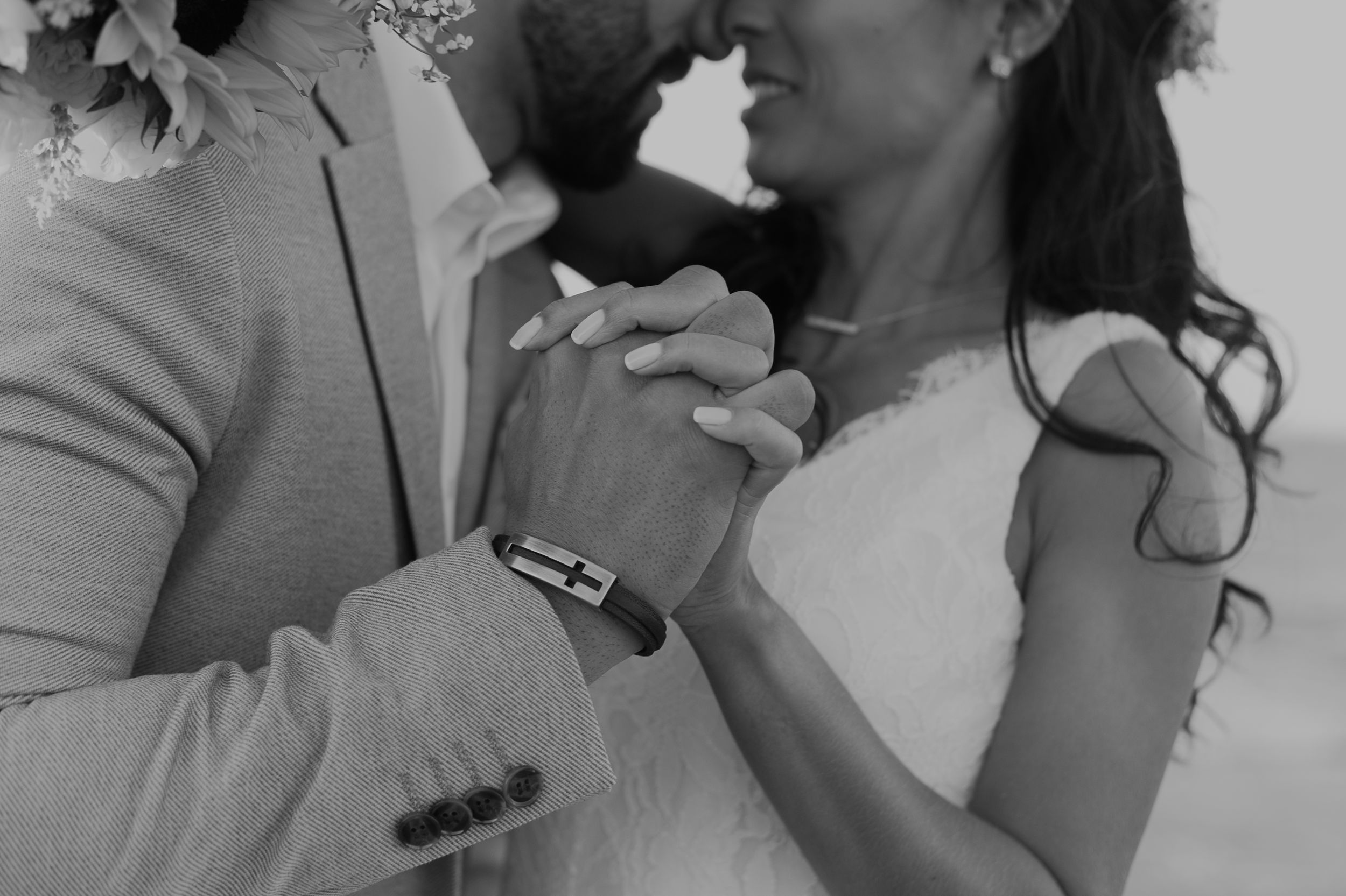 Black and white photo of a couple holding hands during their wedding ceremony.