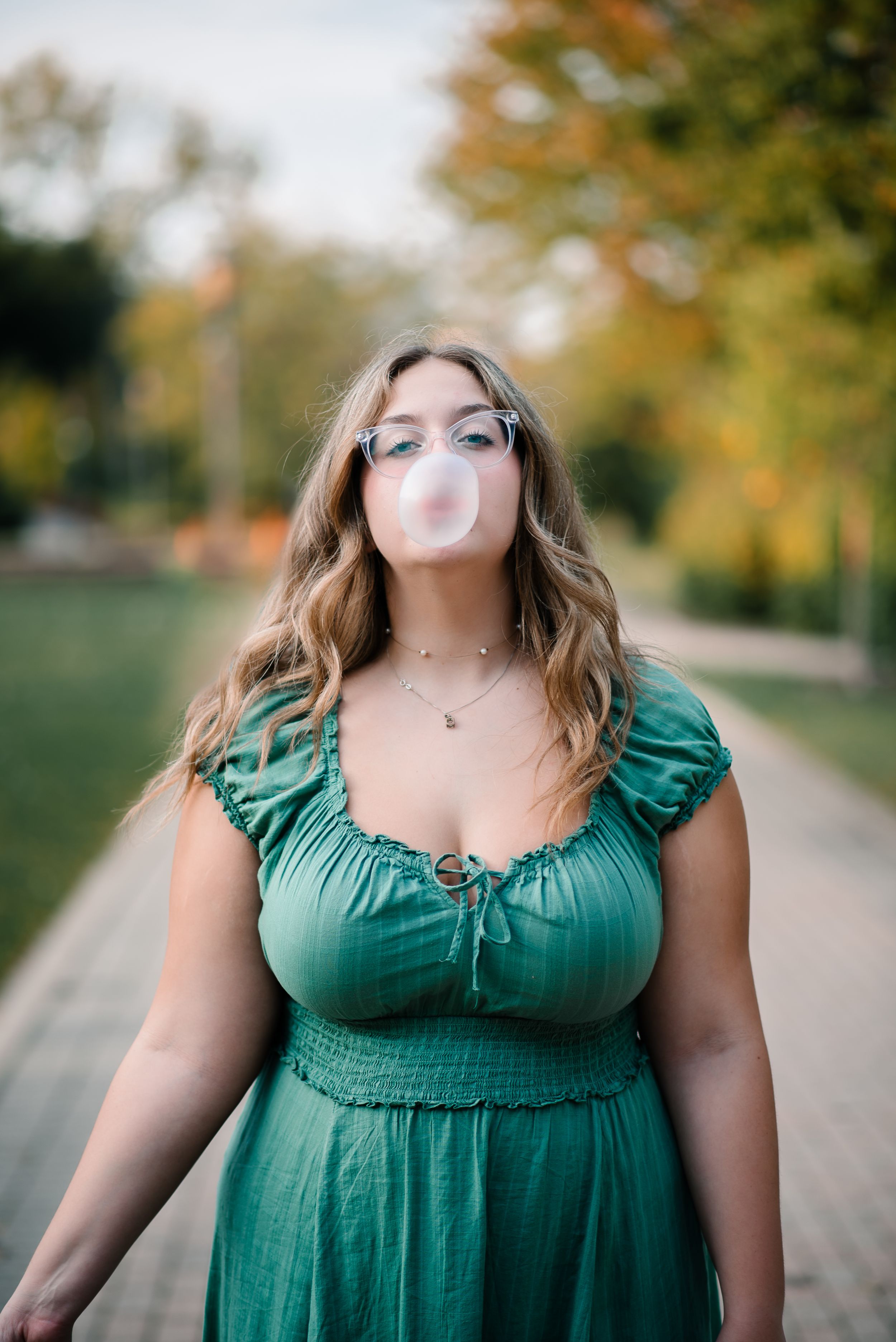 Person in green dress blowing bubble gum in autumn park setting.