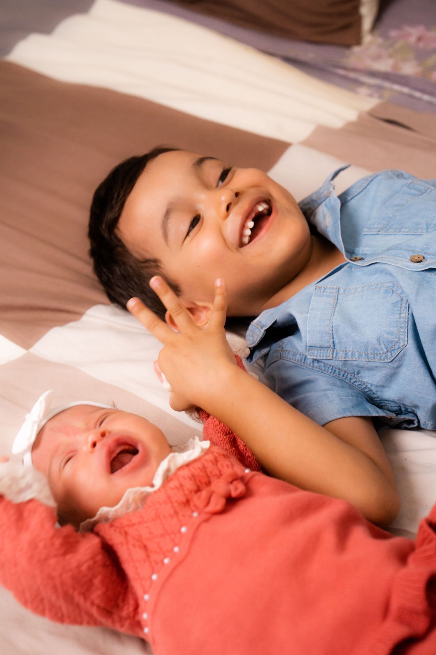Two siblings laying on bed laughing and having fun together.