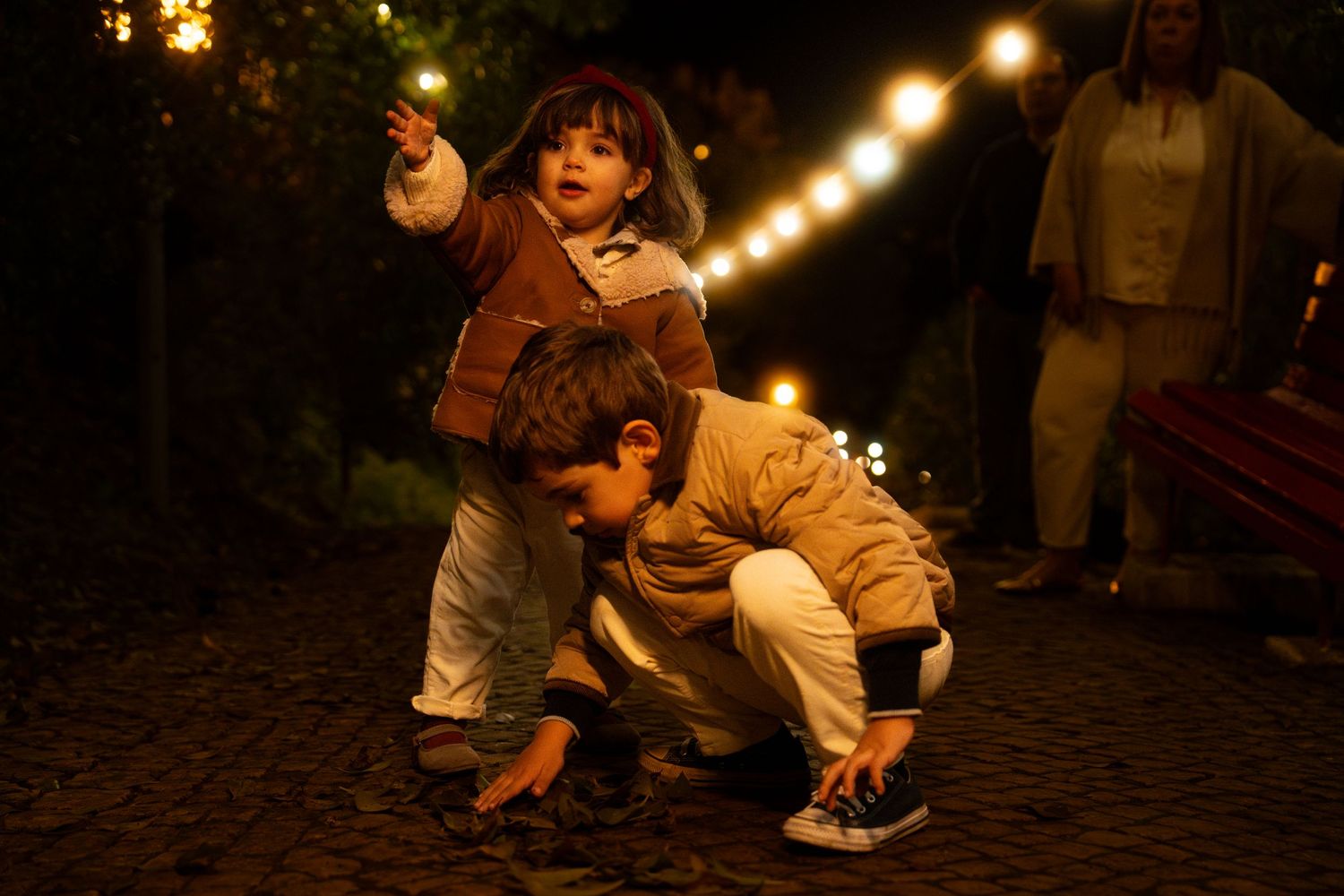 Children playing outdoors at night under string lights creating a magical atmosphere.